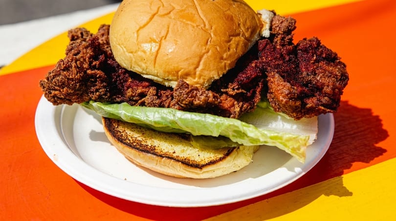 Crispy fried chicken sandwich with lettuce and pickles on a toasted bun, on a white plate.