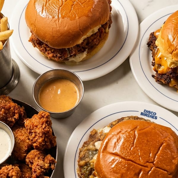A table spread with Disco Birdies burgers, fried chicken, fries, and dipping sauces.