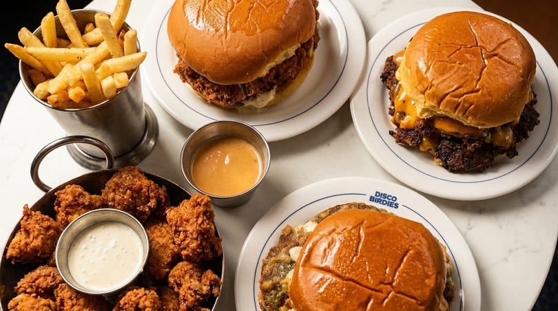 Table spread with Disco Birdies burgers, fried chicken, fries, and dipping sauces.